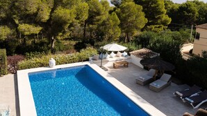 Una piscina rettangolare con acqua cristallina e blu, circondata da un’area relax con divani bianchi e lettini prendisole, e un tavolino.