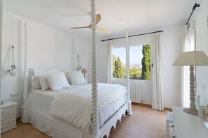 A four-poster bed with a ceiling fan, white bedding, a nightstand with a lamp, and a view of greenery outside. - Villa 'Bonita' with Private Pool, Wi-Fi and Air Conditioning (Capsades)