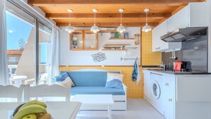 Una cocina compacta con lavadora, zona de comedor con mesa y sofá, y un frutero sobre la mesa.