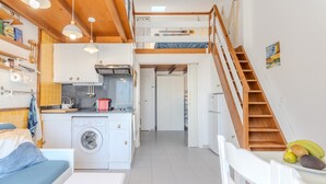 Un espacio habitable compacto con cocina, lavadora, cama y una escalera que lleva a un nivel superior.