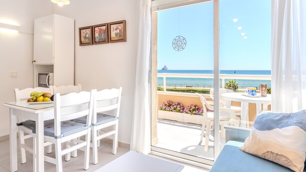 Un balcón con vistas al mar, un área de comedor con sillas y una mesa, y una cama con vistas.