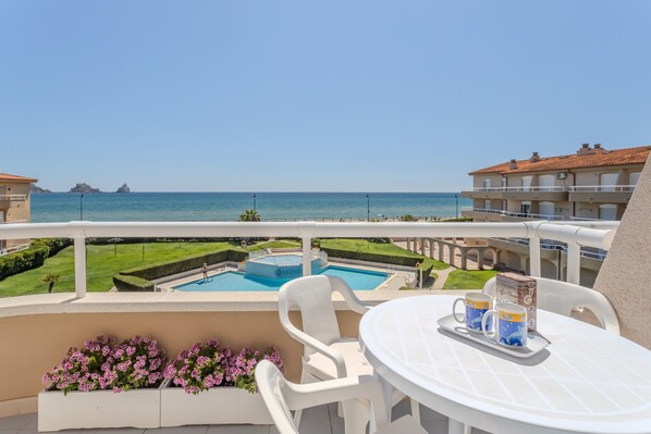 A balcony with a pool, chairs, and a table with mugs.