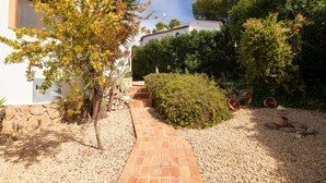 A pathway leading to a building with a white exterior, surrounded by greenery and a gravel area with scattered rocks. - Villa 'Nichola' with Private Pool, Wi-Fi and Air Conditioning (Xàbia)