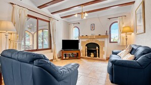 A living room with two blue sofas, a flat-screen TV, a fireplace, and a bookshelf. - Villa 'Nichola' with Private Pool, Wi-Fi and Air Conditioning (Xàbia)