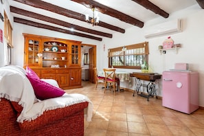 A cozy kitchen with wooden cabinets, a dining table, chairs, a vintage refrigerator, and a window with curtains.