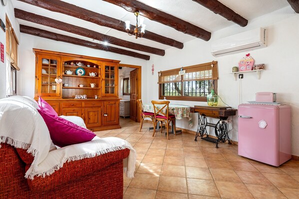 Una cocina acogedora con armarios de madera, una mesa de comedor, sillas, un refrigerador antiguo y una ventana con cortinas.