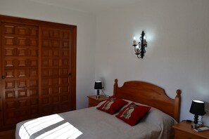 A bedroom with a wooden door, a bed with two pillows, a nightstand with a lamp, and a wall-mounted light fixture. - Villa 'Vicenta' with Private Pool, Wi-Fi and Air Conditioning (Jávea)