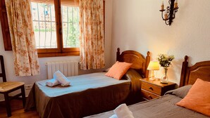 Ein Hotelzimmer mit zwei Betten, einem Sessel, einem Nachttisch mit Lampe und einem fenster mit Vorhängen.