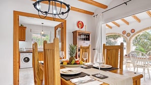 A dining area with wooden furniture, a table set for two, and a view of the kitchen and outdoor space.