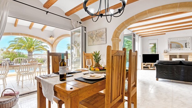 A dining area with a wooden table and chairs, a bottle of wine, and a fruit bowl.
