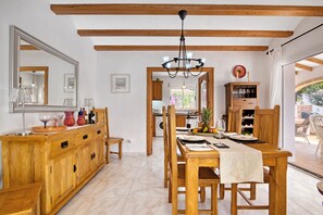 A dining area with wooden furniture, a chandelier, and a view of the kitchen and garden. - Villa 'Margarite' with Private Pool, Wi-Fi and Air Conditioning (Xàbia)