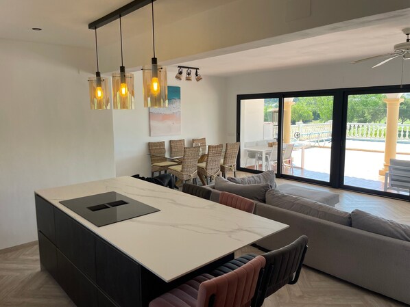 Cozinha moderna com ilha de mármore, iluminação pendente e vista para o pátio externo.