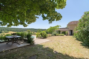 Eine Terrasse mit Tisch, ein Steinhaus und Blick auf die Landschaft.