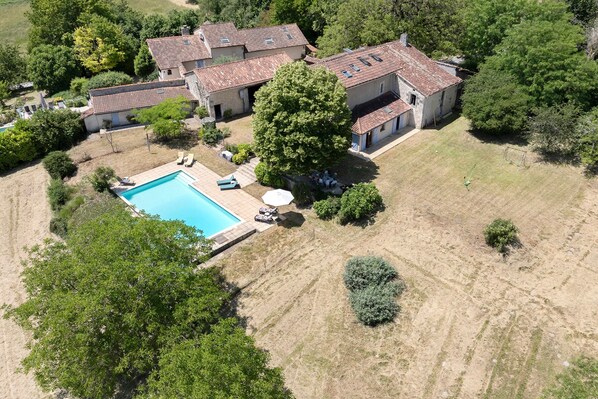 Vue aérienne d’une propriété comprenant une piscine, plusieurs bâtiments et un espace vert environnant.