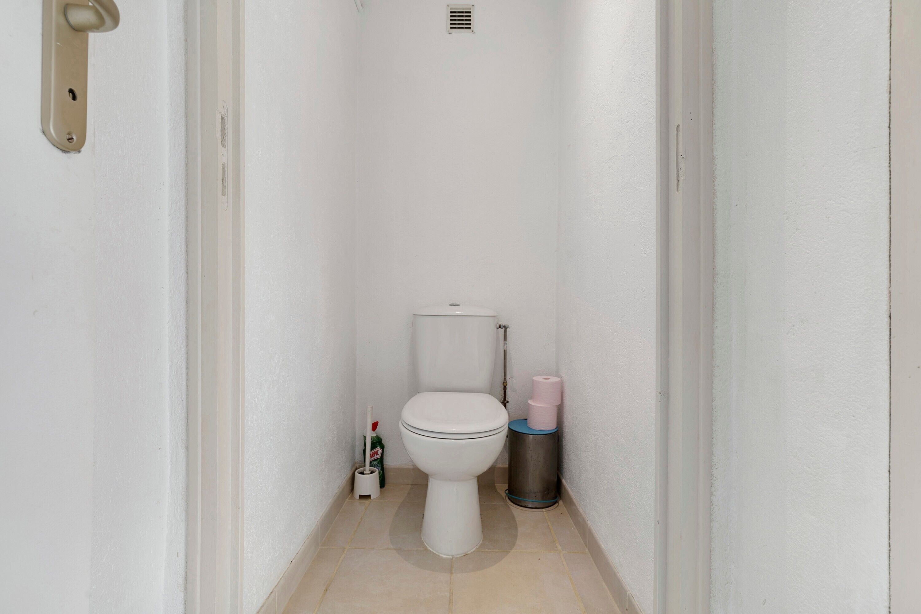 A narrow bathroom with a toilet, a trash bin, and a toilet paper holder.