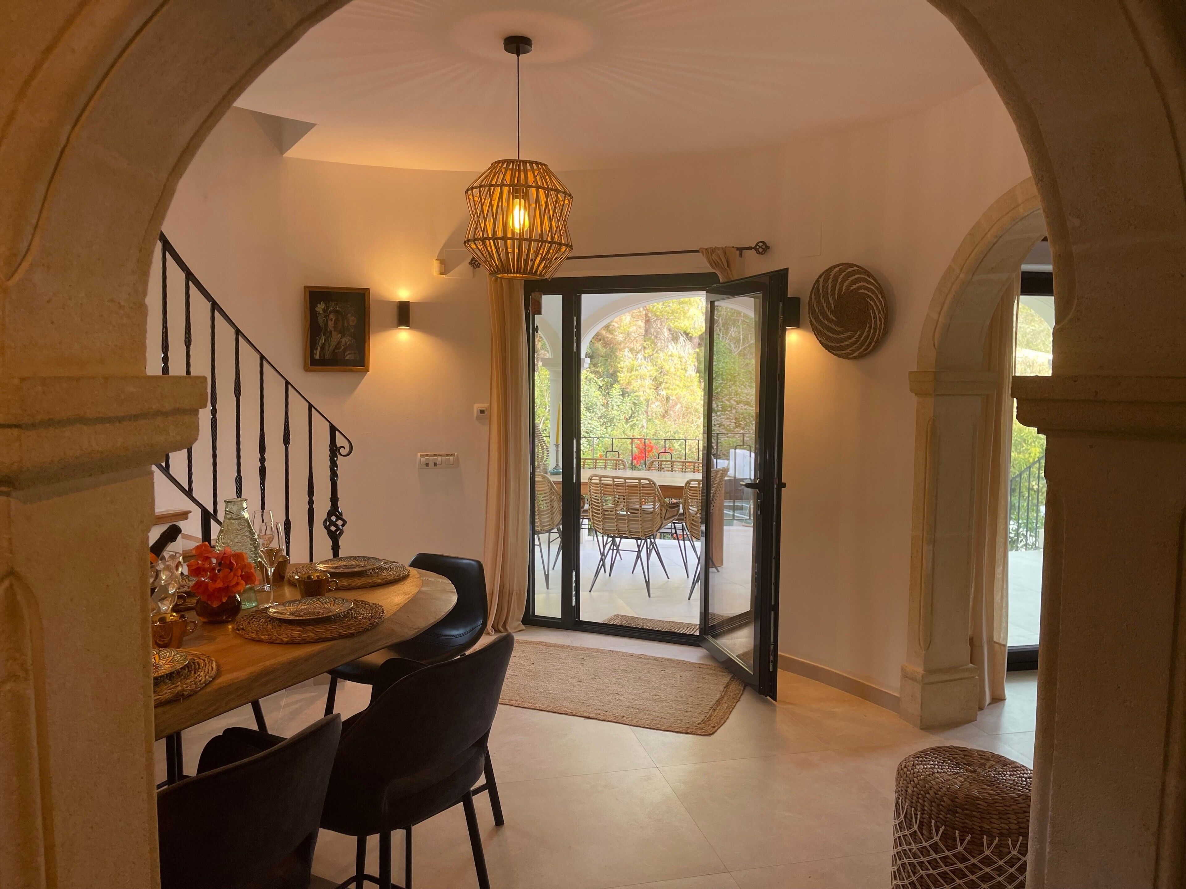 A dining area with a table set for four, a chandelier, and a view through a glass door to an outdoor patio.