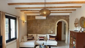 Un salon comprenant un canapé, une table basse ronde en bois, un mur en pierre, un luminaire suspendu et un meuble en bois.