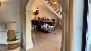 Un espace repas agrémenté d’une arche en pierre, d’un escalier et d’une table entourée de chaises.