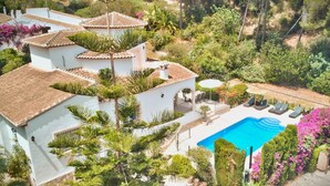 Une villa blanche dotée d’une piscine, entourée d’une végétation luxuriante et agrémentée d’un petit patio.