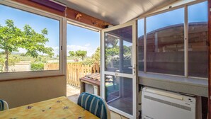 A sunroom with a table and chairs, large windows, and an air conditioning unit. - Holiday Home 'Les Eaux Vives 1' with Sea View, Shared Pool and Private Terrace (Fleury)