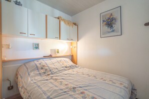 A bedroom with a bed, a nightstand, a shelf with decorative items, and a framed painting on the wall.