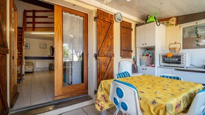 A cozy kitchen with a dining table, a ceiling fan, and a window with curtains. - Holiday Home 'Les Eaux Vives 1' with Sea View, Shared Pool and Private Terrace (Fleury)