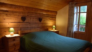 A wooden room with a bed, two bedside tables with lamps, a window with curtains, and two heart-shaped wall decorations.