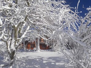 Un paysage enneigé avec un bâtiment en bois, vraisemblablement un chalet, entouré d’arbres.
