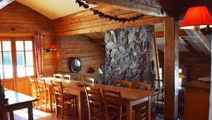 A wooden interior with a stone wall, wooden table, chairs, and a clock.