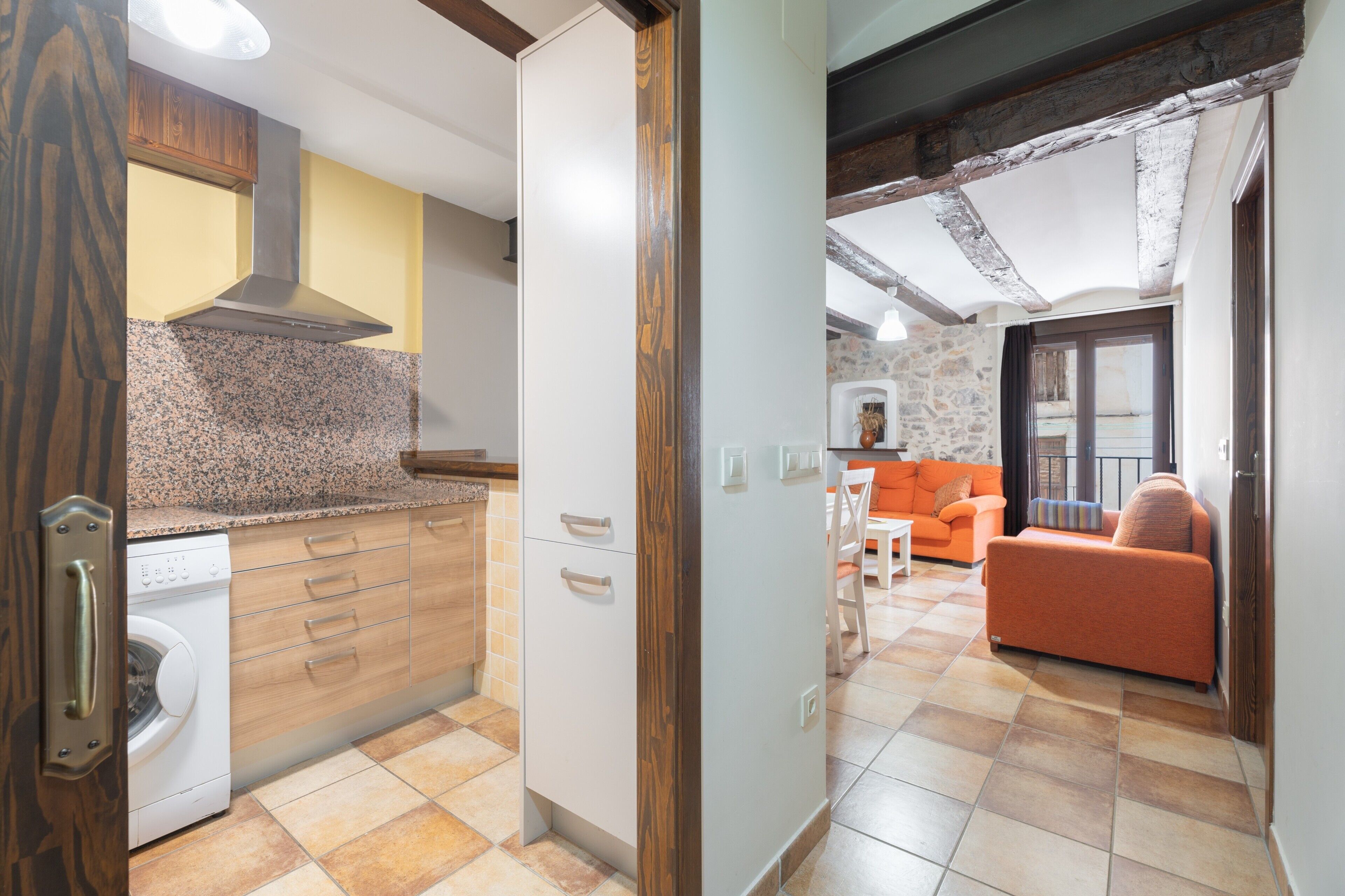 A kitchen with a washing machine, wooden cabinets, and a stone wall.