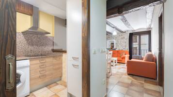 A kitchen with a washing machine, wooden cabinets, and a stone wall.