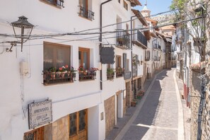 Una calle estrecha con edificios blancos, balcones con plantas en macetas y letreros que indican 'APARTMENTS CORELLA' y 'BAR Restaurant Corella'.