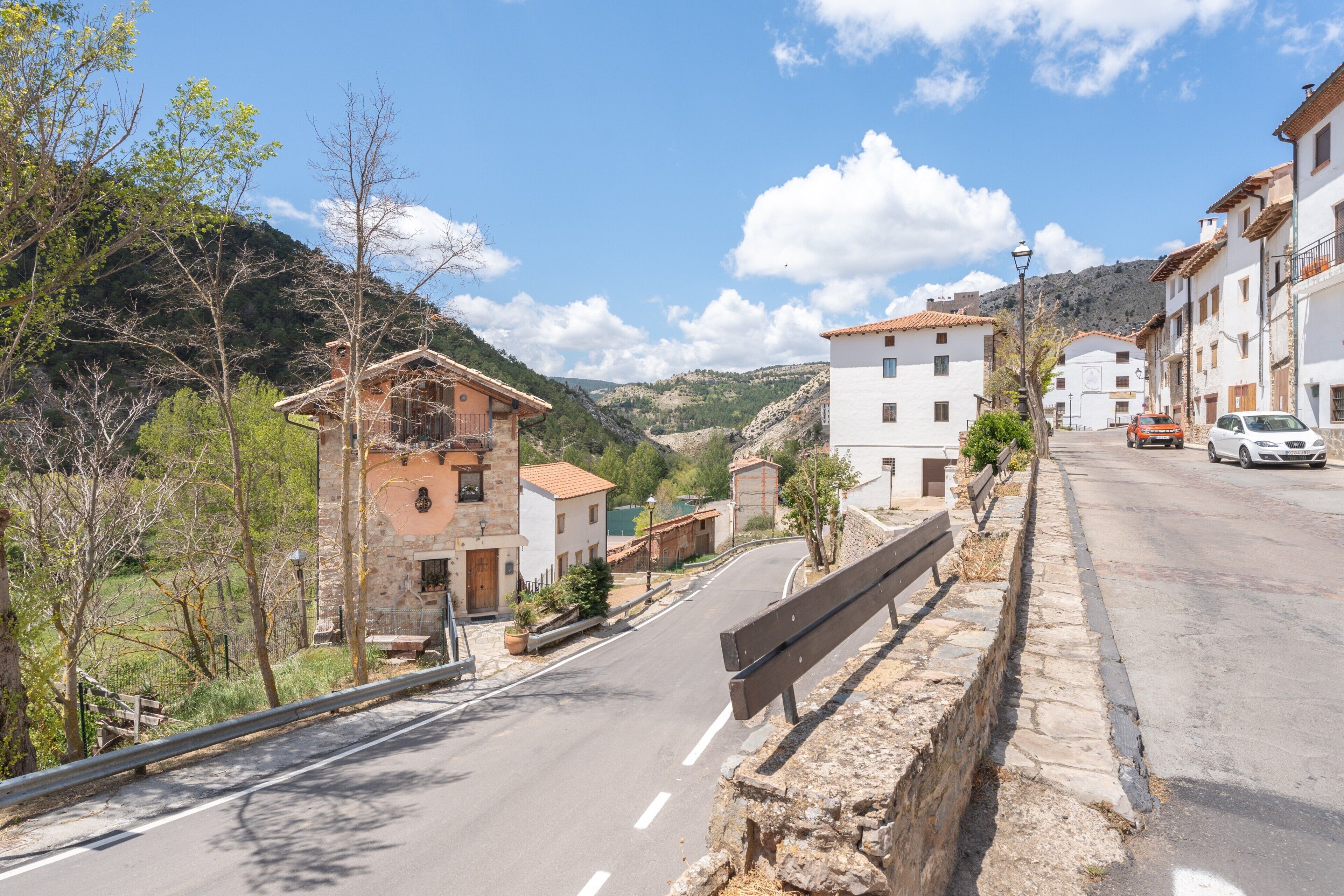 Calle con edificios de piedra, una banca y un coche en la vía.