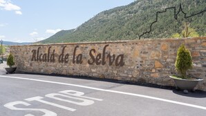 Un mur de pierre sur lequel on peut lire « Alcalá de la Selva », une aire de stationnement avec un panneau « STOP », et une montagne en arrière-plan.