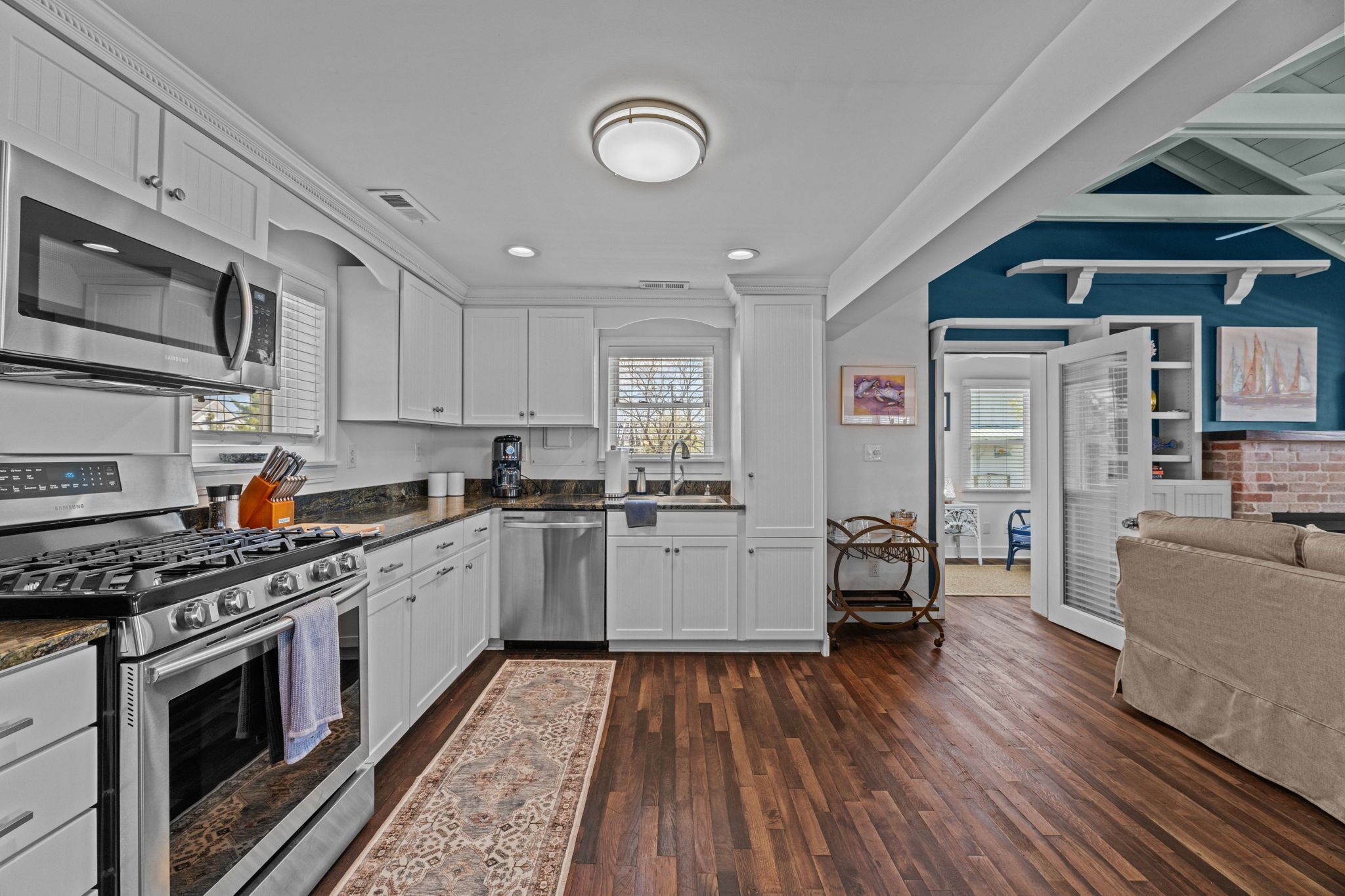 A modern kitchen with white cabinetry, stainless steel appliances, and a wooden floor.