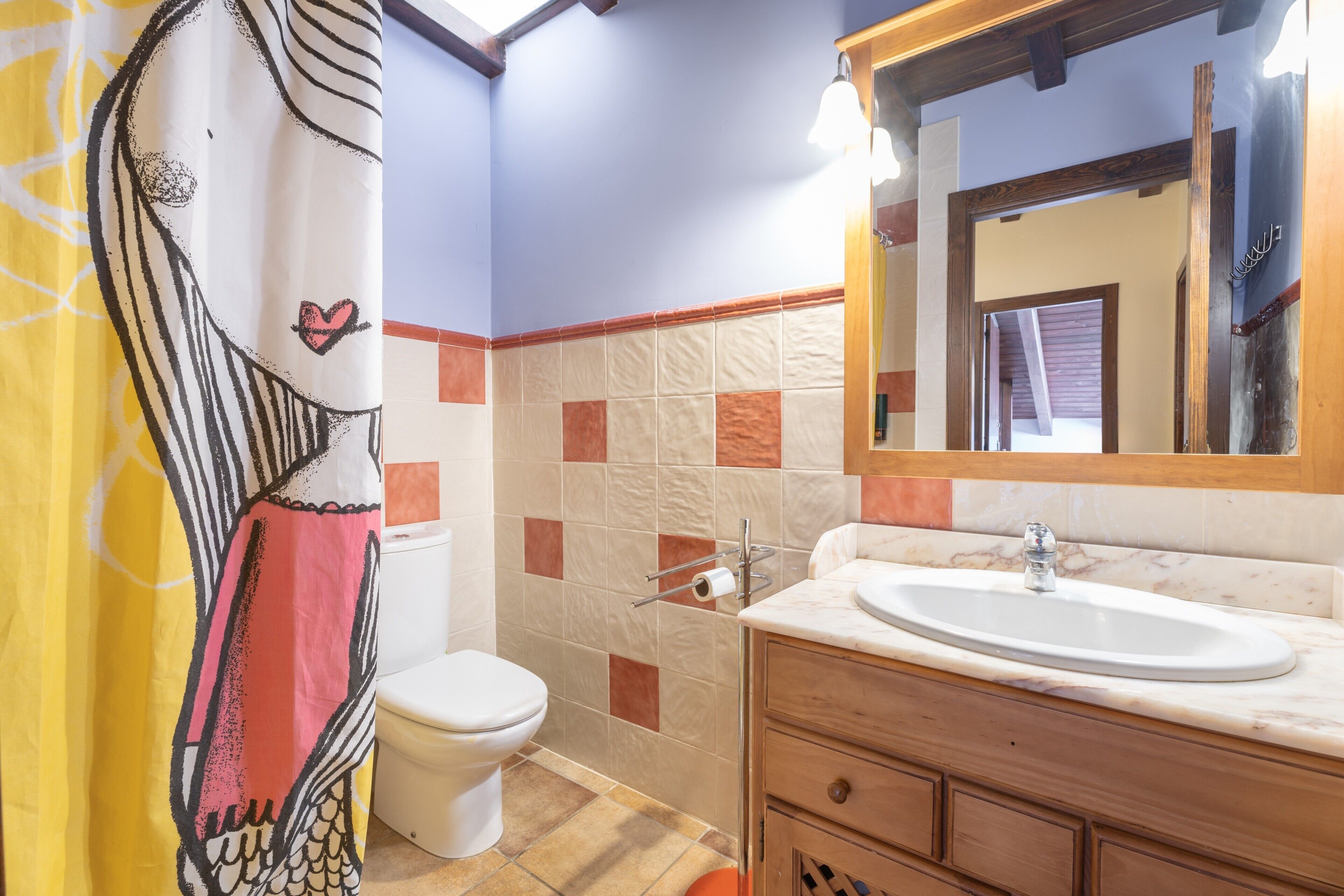 A bathroom with a toilet, sink, mirror, and shower curtain.