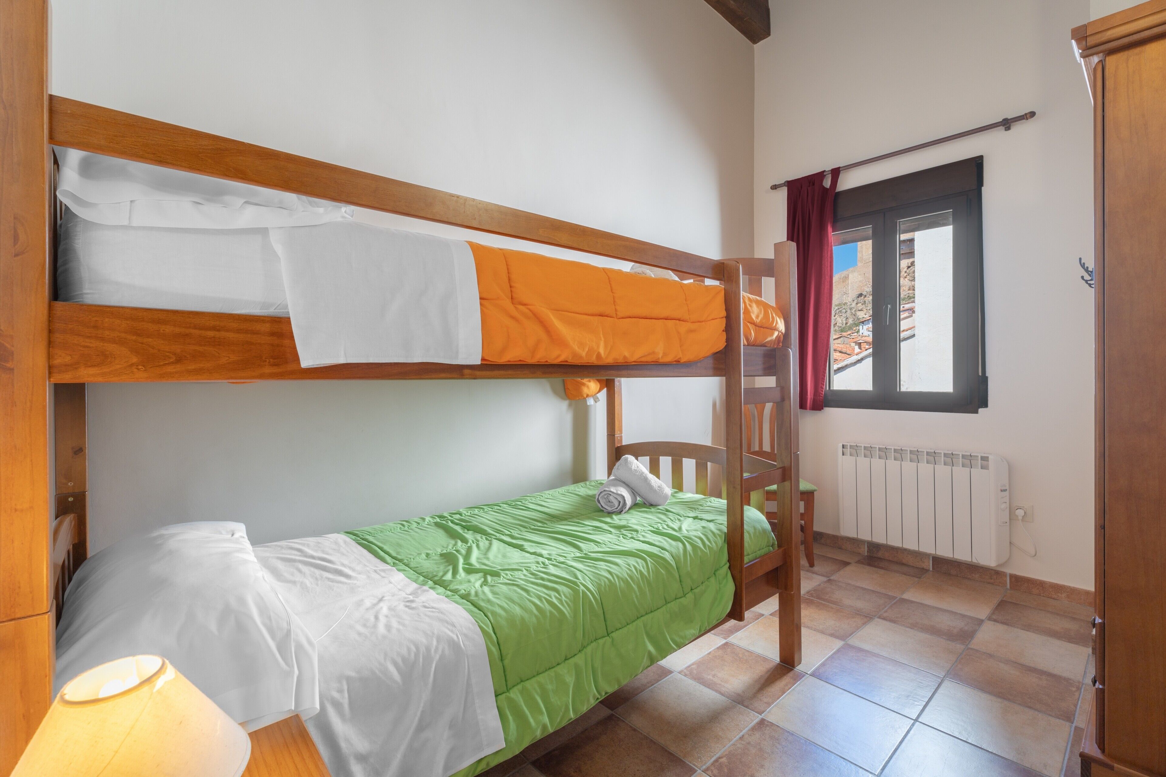Dormitorio con literas, un edredón verde, un edredón blanco y una escalera de madera.