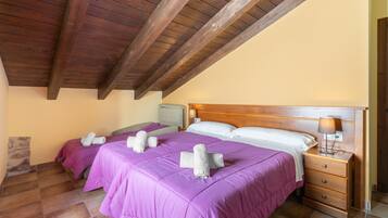 A bedroom with two beds, wooden headboards, a nightstand with a lamp, and a stone wall.