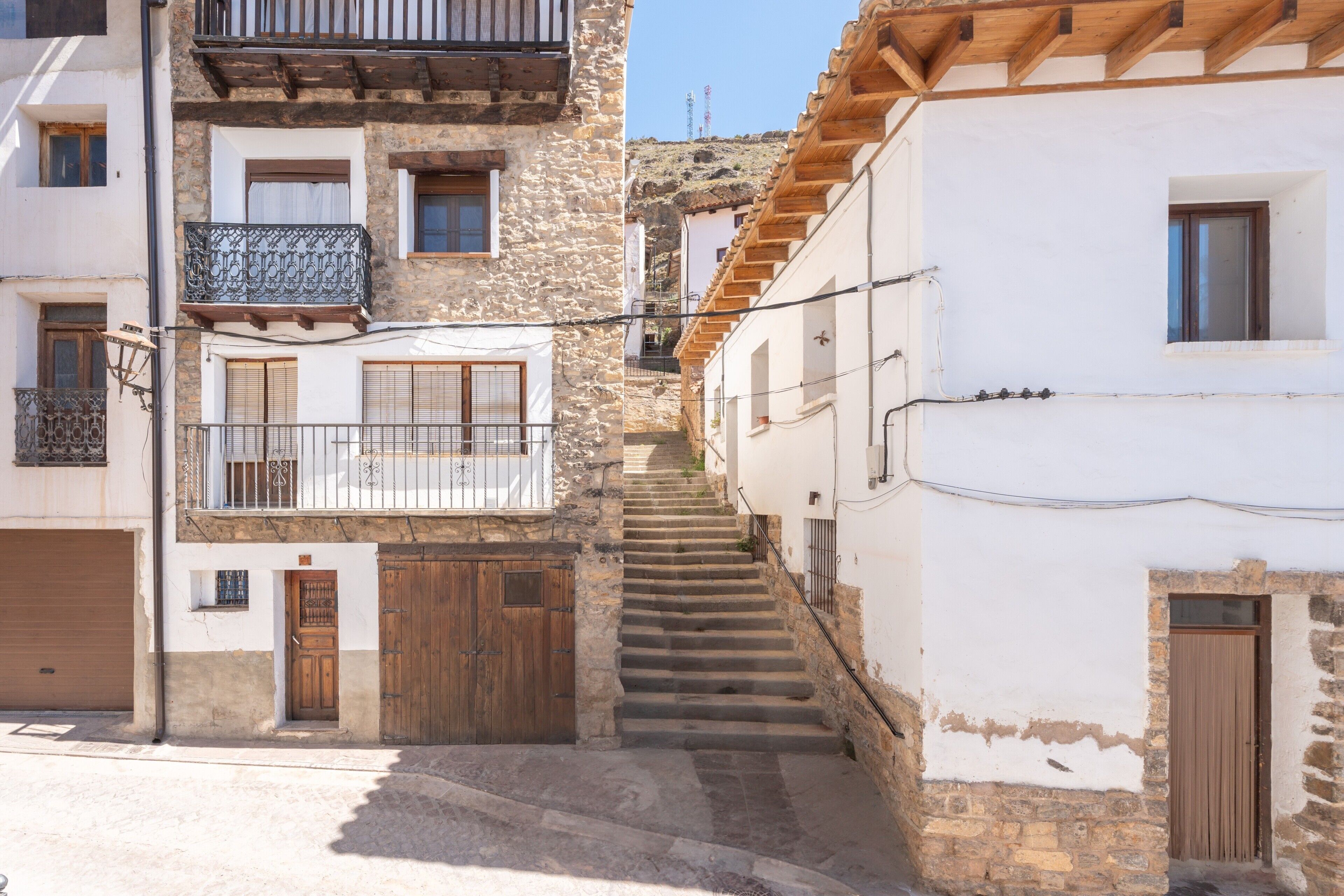 Una calle estrecha con edificios de piedra, puertas de madera y una escalera que sube a un nivel superior.