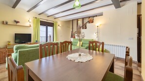 A dining area with a wooden table, chairs, a television, and a green sofa.