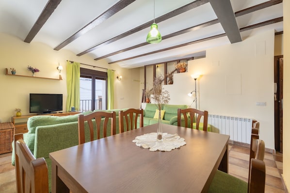 A dining area with a wooden table, chairs, a television, and a green sofa.