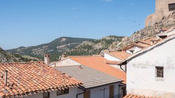 Blick auf terrakottafarbene Dächer, ein Gebäude mit einer Steinmauer und eine gebirgige Landschaft im Hintergrund.