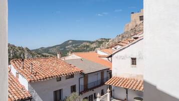 Vista de un pueblo en la ladera de una colina con edificios de tejas de arcilla, un edificio blanco destacado con balcón y una montaña distante.