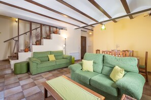 A living room with two green sofas, a wooden coffee table, and a staircase with wooden beams.