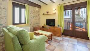 A living room with a green sofa, a television, a wooden cabinet, and a window with curtains.