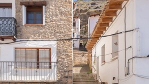 A stone building with a wooden balcony, a staircase leading to a higher level, and a white building with a wooden roof.