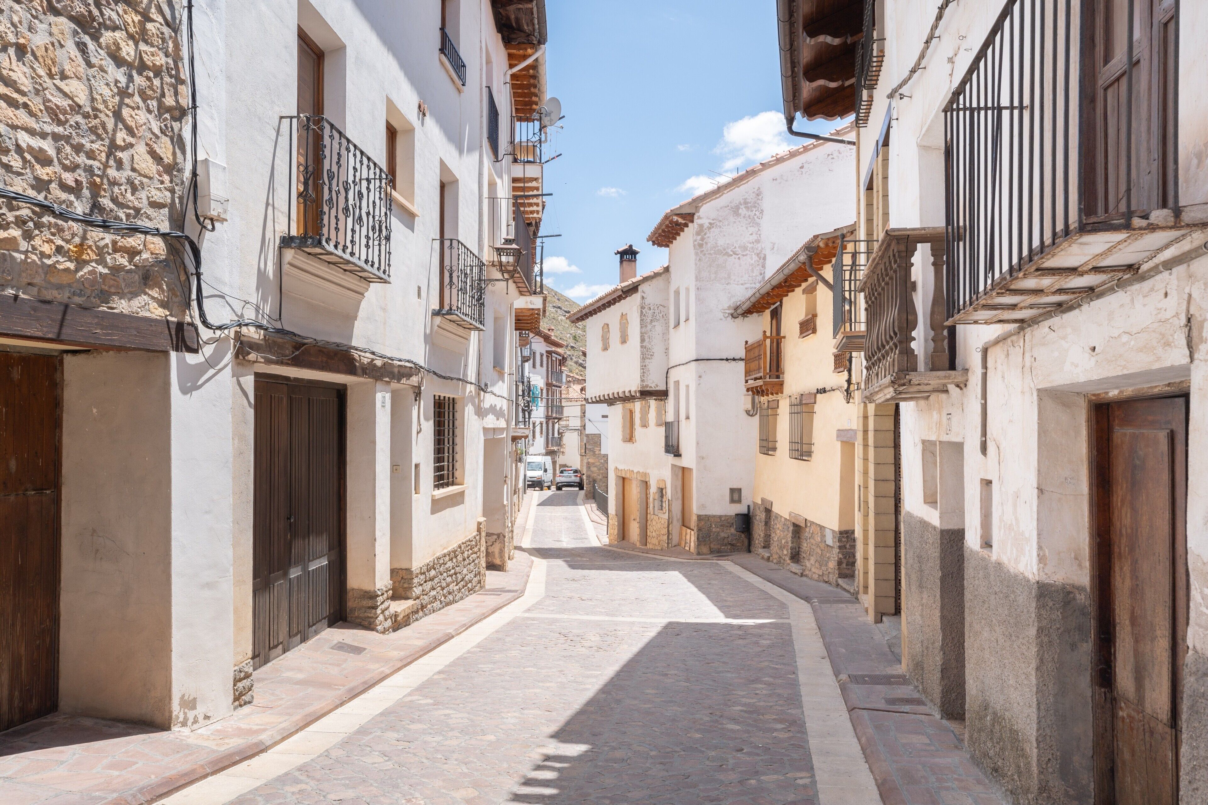 Una calle estrecha bordeada de edificios tradicionales, con muros de piedra, puertas de madera y balcones.