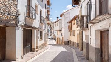 Una calle estrecha bordeada de edificios tradicionales, con muros de piedra, puertas de madera y balcones.