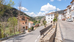 Calle con edificios de piedra, una banca y un coche en la vía.