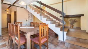 Un comedor con una mesa y sillas de madera, una escalera de piedra y una lámpara fijada a la pared.